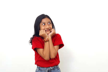 Happy asian little girl standing while dreaming or thinking something. Isolated on whiteの写真素材