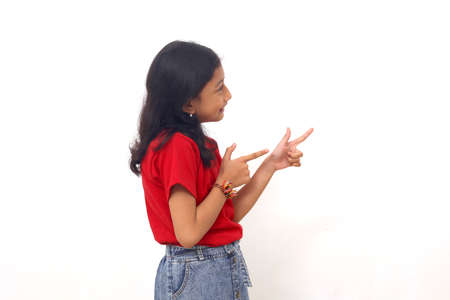 Happy asian little girl standing while pointing something sideways. Isolated on white with copyspace