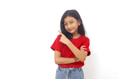 Happy asian little girl standing while pointing something sideways. Isolated on white with copyspace