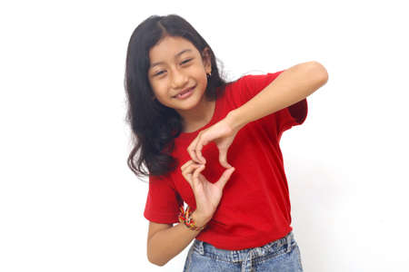 Cheerful asian little girl standing while showing love shape with her hands. Isolated on white