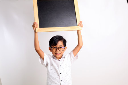 Happy asian schoolboy standing while showing a blank blackboard. Isolated on white backgroundの写真素材