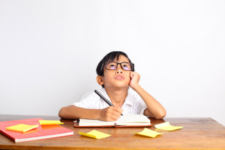Asian schoolboy studying and thinking on the desk. Isolated on white backgroundの写真素材