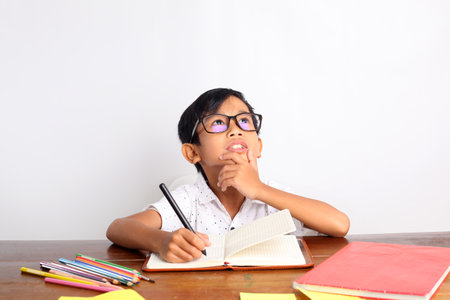 Thoughtful asian schoolboy studying in classroom while looking up. Isolated on white background