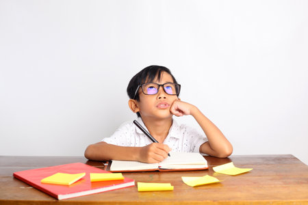 Asian schoolboy studying and thinking on the desk. Isolated on white backgroundの写真素材