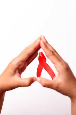Woman's hand and red ribbon over white with copyspace. Aids day concept