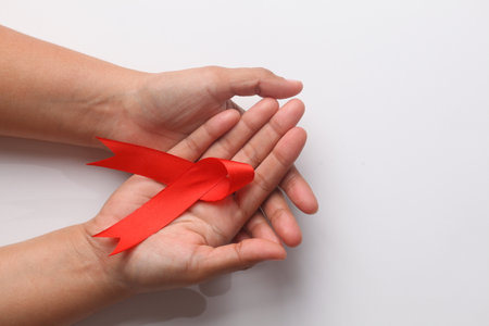 Close up photo of woman's hand holding red ribbon over white background with copyspace. Aids day...