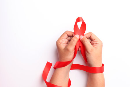 Close up photo of woman's hand holding red ribbon over white background with copyspace. Aids day...