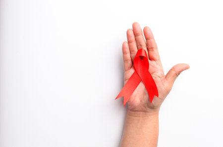 Close up photo of woman's hand holding red ribbon over white background with copyspace. Aids day...