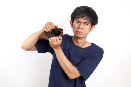Disappointed young asian man standing while opening his empty wallet. Isolated on white background