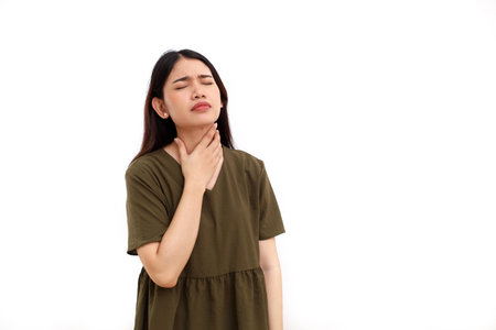 Beautiful young asian woman standing while holding her neck. She suffering from sore throat....