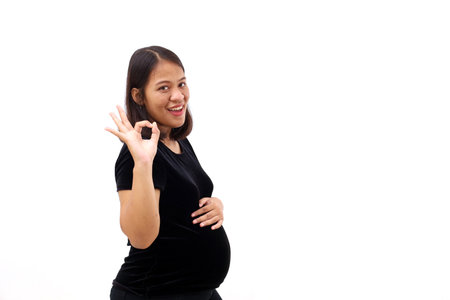 Asian pregnant woman smile with big belly while showing okay hand gesture. Isolated on white backgroundの写真素材