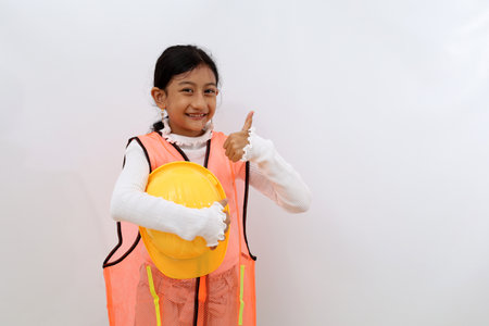 Happy Asian little girl in the construction helmet as an engineer standing while showing thumbs up. Isolated on white with copyspaceの写真素材