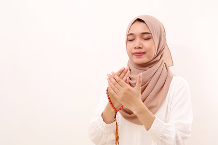 Young asian muslim woman praying and holding prayer beads. Isolated on white with copyspace