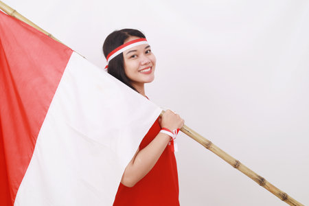 Young indonesian girl celebrate independence day while holding red white flag. Isolated on whiteの写真素材