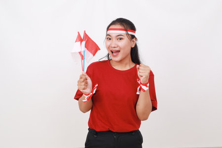 Excited young indonesian girl holding red white flag while clenched hand. Isolated on whiteの写真素材