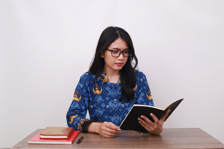 Beautiful Asian female in batik korpri, indonesian traditional worker uniform reading a bookの写真素材