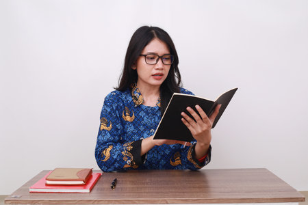 Confused Asian female in batik korpri, indonesian traditional worker uniform reading a bookの写真素材