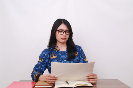 Confused Asian female in batik korpri, indonesian traditional worker uniform holding papersの写真素材
