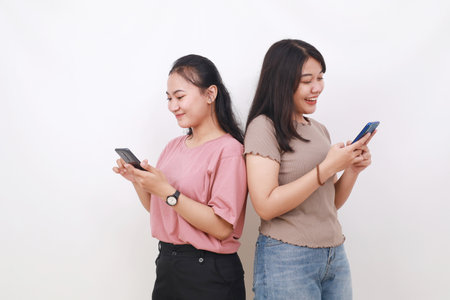 Two asian women hold in hand use cell phone browsing internet chatting online isolated on whiteの写真素材