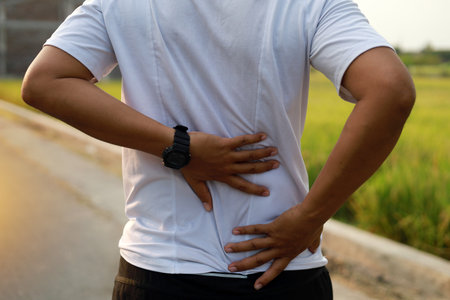 Close up photo of Asian Man with back pain during doing outdoor exercise.の写真素材
