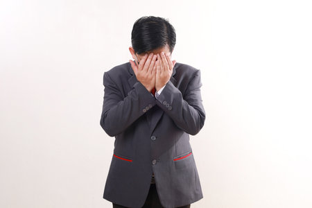 Stressed asian businessman standing while covering face. Isolated on white background