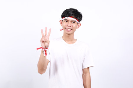 Asian young boy with red white ribbon for celebrating Indonesia independence day standing while showing three fingersの写真素材