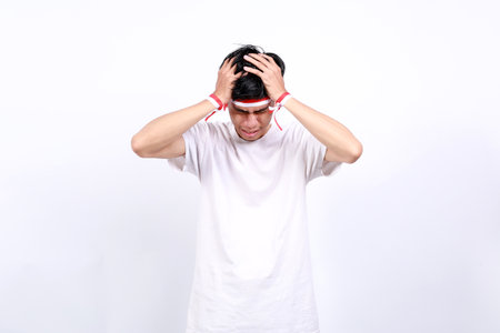 Stressed Young asian boy with red white ribbon celebrating Indonesia independence day while holding his headの写真素材