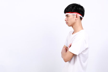 Side view of Young asian boy with red white ribbon celebrating Indonesia independence day while looking sideways and thinking somethingの写真素材