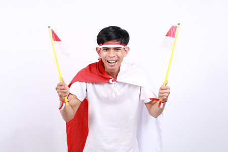 Excited Asian young boy with red white ribbon for celebrating Indonesia independence day standing while holding Indonesia flagの写真素材
