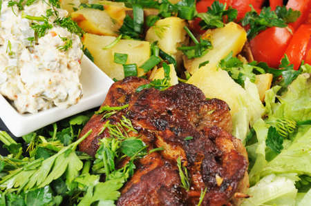 Grilled meat and potatoes. Decorated with tomatoes, lettuce and herbs.