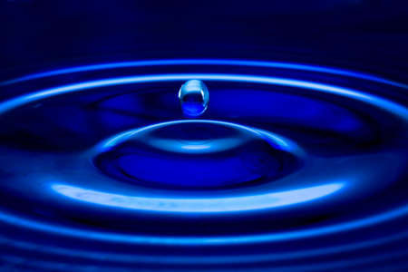 The water drop falls in dark blue water with dispersing circles close upの写真素材