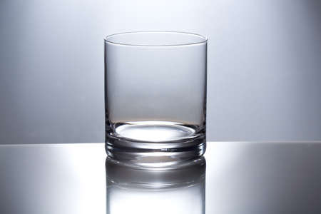 The empty transparent glass glass for whisky is reflected in a glass table