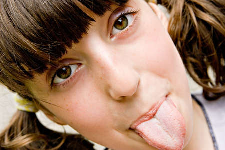 The brown-eyed dark-haired girl-teenager looks directly in a shot and puts out the tongue 