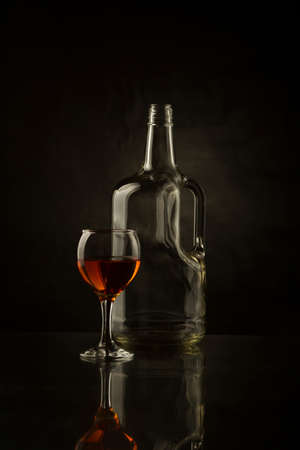 A bottle and a glass of alcohol on darkの写真素材