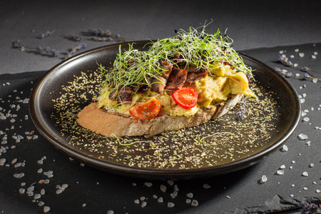 Bruschetta with omelette, green sprouts, ham and tomatoes on a dark backgroundの写真素材