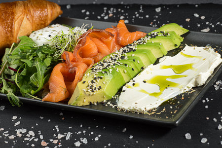 Italian panini sandwich, french croissant with salmon, avocado, rukkola and cream cheese on a rectangle plateの写真素材
