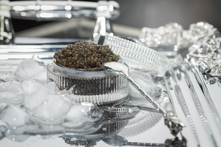 Black caviar. Black sturgeon caviar in a cut-glass bowl and a metal spoon on a silver tray filled with ice.の写真素材