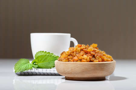 Raisins in a wooden bowl and a cup of tea or coffee with mintの写真素材