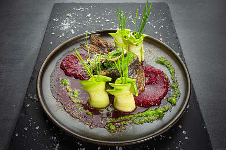 Decorated fish roll with sliced zucchini and red beet puree garnish on dark restaurant dish. Original presentationの写真素材