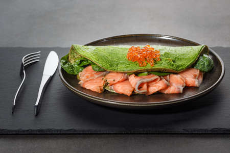 Green spinach omelet with samon and caviar on a dark plate.の写真素材