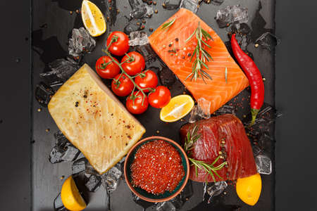 Caviar, smoked salmon, tuna, hausen and vegetables on a black board with ice.