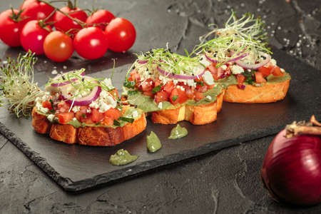 Fresh delicious bruschetti. Variety of small sandwiches with fresh vegetables, ricotta and green sauce over dark backgroundの写真素材