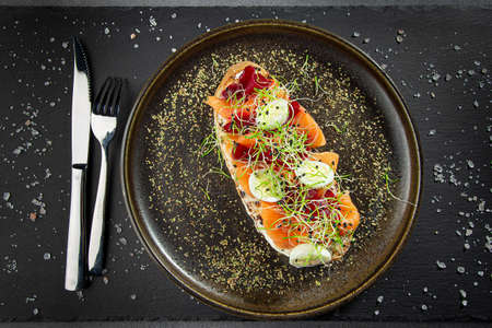 Bruschetta with salmon, beet slices, quail eggs and sprouts on a dark backgroundの写真素材