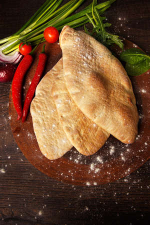 Whole pita with vegetables on wooden background. Top view