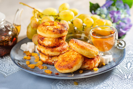 Fried cottage cheese pancakes syrniki with raisins and grapes on a blue dish served with black tea.の写真素材