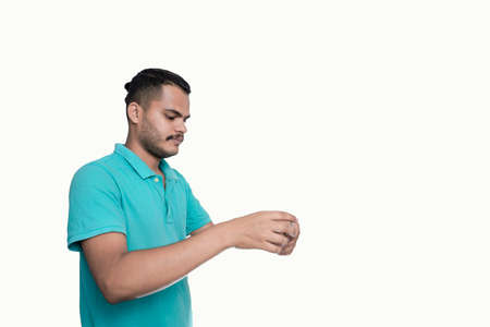 Young man in blue polo t-shirt looking at wristwatch on white backgroundの写真素材