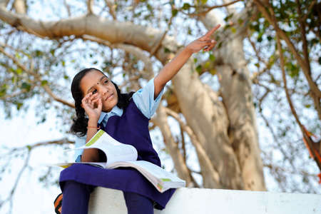 Smiling student girl wearing school backpack and holding exercise book. Portrait of a happy asian young girl outside the primary school. Closeup face of smiling schoolgirl looking at camera.の写真素材