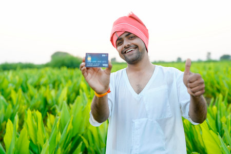Young indian farmer showing debit or credit card at his green agriculture fieldの写真素材