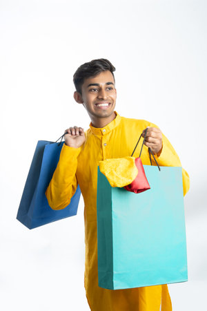 Happy handsome indian man wearing traditional outfit shopping bag celebrating diwali festival isolated on studio backgroundの写真素材