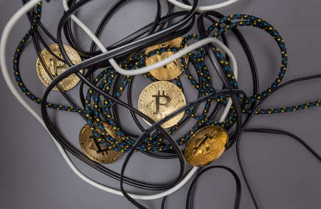 Bitcoin gold coins trangled in a nest of cables on a grey background